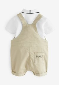 Vaaleat haalarit valkoisen kauluspaidan kanssa, jossa on musta kaulust accentti ja takatasku, jossa lukee 'BAKER'.