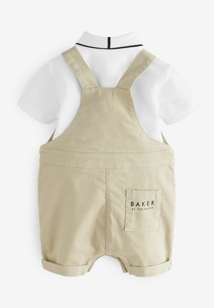 Salopette beige avec une chemise blanche à col en dessous, présentant un col noir accentué et une poche arrière avec "BAKER" imprimé dessus.