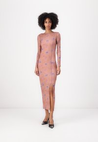 Long-sleeve, fitted dress in soft pink fabric with blue patterns. Features a thigh-high slit and round neckline, paired with black heels.