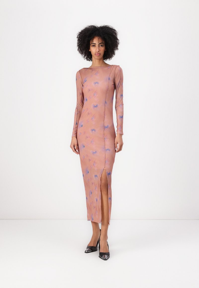 Long-sleeve, fitted dress in soft pink fabric with blue patterns. Features a thigh-high slit and round neckline, paired with black heels.