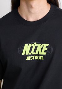 Henkilö, joka on pukeutunut mustaan paitaan, jossa on neonkeltainen Nike-logo ja "Just Do It" -slogan keskitettynä rintaan.
