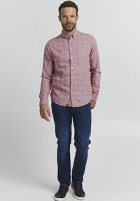 Rød og grå rutete skjorte med knappelukking og brystlomme, kombinert med blå jeans og svarte sneakers. Skjorten har lange ermer og krage.