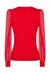 Pull rouge ajusté avec des manches longues bouffantes en voile présentant un motif subtil à pois et des poignets boutonnés avec de petits boutons en forme de cœur.