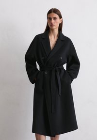 Black double-breasted coat made of wool blend, featuring a belt, wide notched collar, and long sleeves with a relaxed fit.