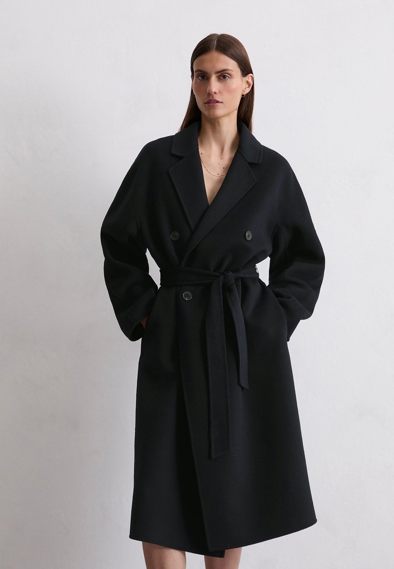 Black double-breasted coat made of wool blend, featuring a belt, wide notched collar, and long sleeves with a relaxed fit.