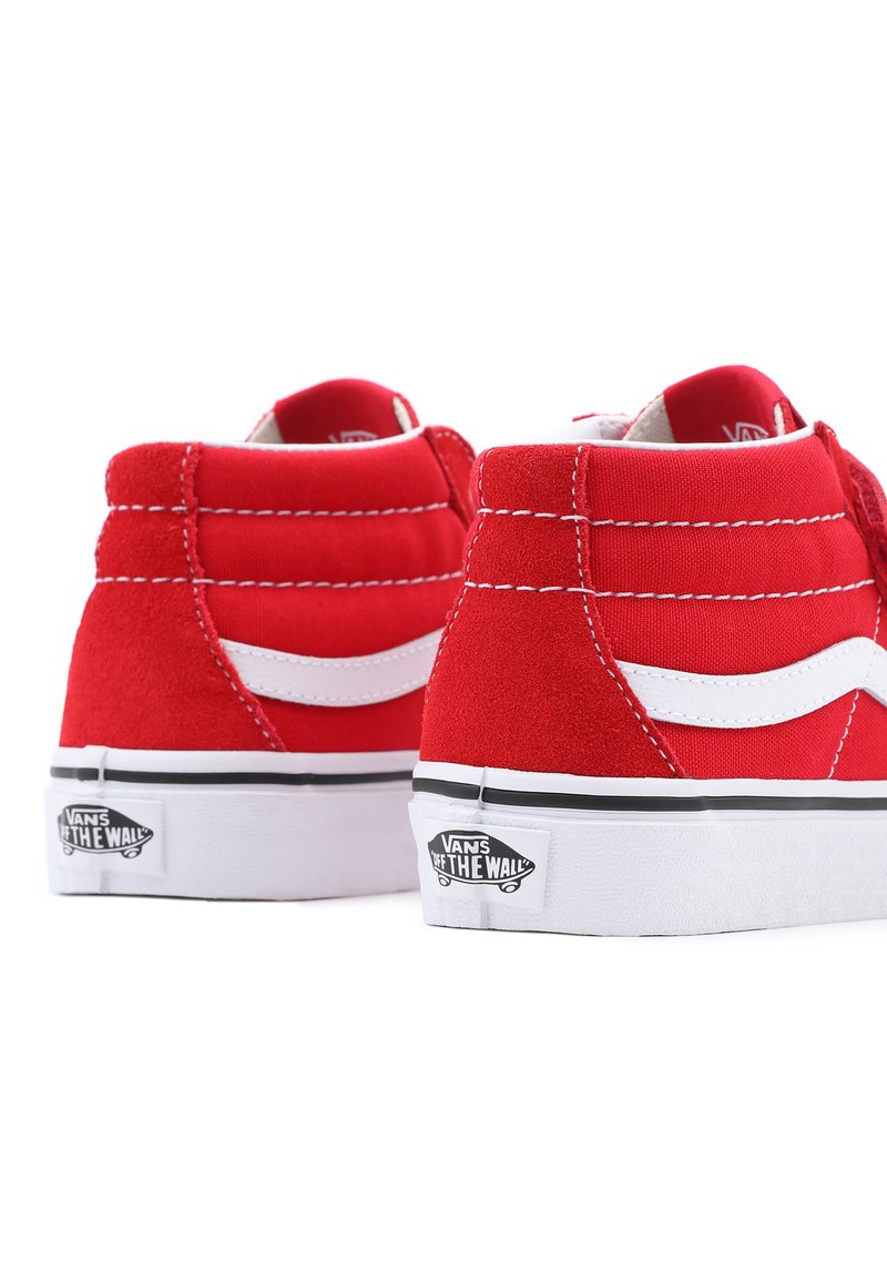 Baskets montantes rouges en daim avec des accents blancs, présentant une rayure classique de Vans et une semelle en caoutchouc noir avec un détail de logo sur le talon.