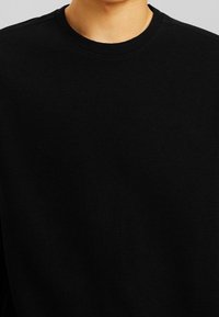 Black long-sleeve shirt with a ribbed texture, featuring a round neckline and no visible logos or embellishments.