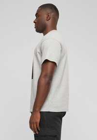 Camiseta de algodón gris con mangas cortas y cuello redondo, exhibida junto a pantalones cargo negros, sobre un fondo neutro.