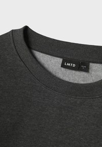 Sudadera gris oscuro con cuello redondo acanalado, forro interior suave y una etiqueta que dice "LMTD" con información de tamaño visible.