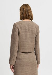 Blazer marrón con textura, de silueta estructurada, que presenta mangas largas, cuello redondo y un diseño cropped.