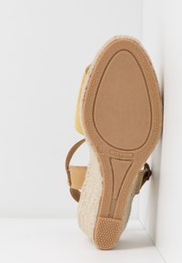 Semelle d'une sandale compensée beige avec une semelle en caoutchouc texturé, taille 37, et étiquette "Fabriqué en Espagne" sur la semelle.