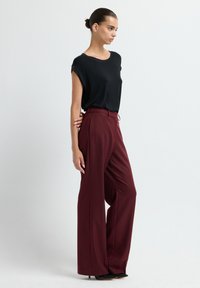 Zwarte t-shirt met korte mouwen gecombineerd met bordeauxrode wijde broek. De broek heeft een hoge taille en een soepele textuur. Beide kledingstukken hebben een losse pasvorm.