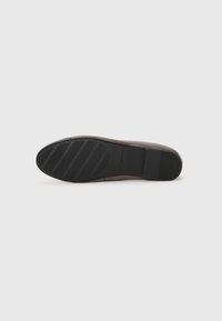 Sole of a brown flat shoe with black rubber grip and brand name embossed on the arch area against a plain white background.