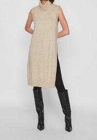 Beige ärmlös polokragsklänning med ribbat fåll, med en avslappnad passform och sidslitsar, i kombination med knähöga svarta stövlar.