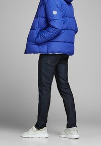 Niebieska pikowana kurtka puchowa z naszywką z logo, w zestawieniu z ciemnymi dżinsami i jasnymi sneakerami.