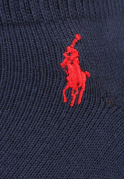 Tissu en maille bleu marine comportant un logo de cheval brodé rouge. La texture est côtelée, soulignant son design tricoté.