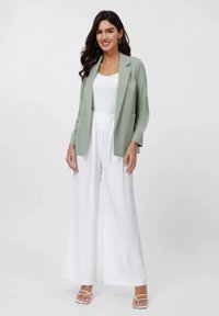 Blazer verde-claro sobre uma blusa branca, combinado com calças largas brancas. Tecido suave com um corte descontraído e bolsos frontais.