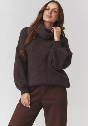 Ciemnobrązowy, oversize sweter z golfem, wykonany z miękkiego materiału, z prążkowanymi mankietami. Noszony z brązowymi spodniami o luźnym kroju i fakturowanym wykończeniu.