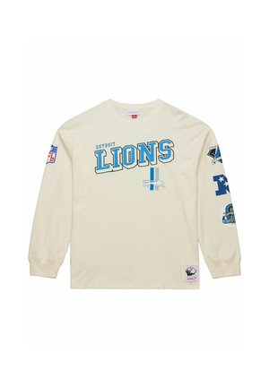 Cremefarbenes Langarm-T-Shirt mit "Detroit Lions" in blauer Schrift. Mit Team-Logos auf den Ärmeln und einem Patch am unteren Ende. Aus Baumwollmaterial.