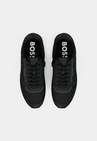 Paire de baskets noires de la marque BOSS avec lacets, vues de dessus sur un fond clair uni.