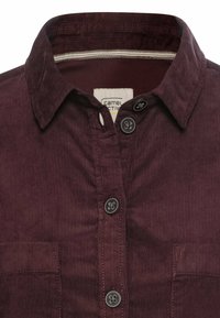 Bordeaux fløjlsskjorte med spids krave, frontknapper og brystlomme. Har en diskret ribbet tekstur og kontrasterende indvendig trim.