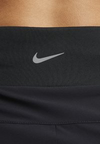 Juodas sportinis juosmuo su lygiu paviršiumi, priekyje yra mažas sidabrinis Nike logotipas. Siuvimo detalės matomos palei kraštą.