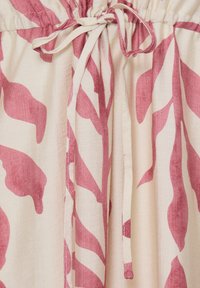 Tissu crème avec motifs de feuilles rose pâle et un cordon noué en nœud papillon à la taille froncée d’un vêtement.