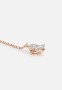 Collier en or rose avec une chaîne et un pendentif au design courbé, orné de cristaux clairs ronds le long du dessus.