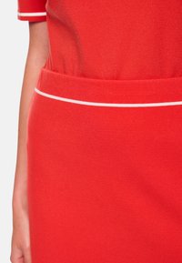 Rotes Baumwollkleid mit figurbetontem Schnitt und einem weißen Akzentstreifen entlang der Taille. Weiche Textur, kurze Ärmel und abgerundeter Ausschnitt.