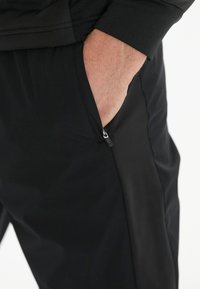 Svarta träningstights med en zip-fick på sidan, slät textur och en tight passform, som visar upp ett lätt och flexibelt tyg.