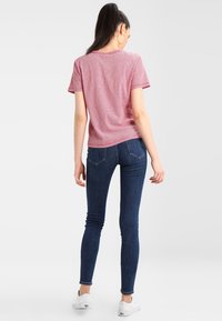 Camiseta de manga corta a rayas rojas y blancas, de tela de algodón, con un corte relajado, combinada con jeans skinny de mezclilla azul y zapatillas blancas.