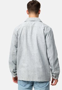 Light gray button-up jacket with a textured fabric, spread collar, and two buttoned cuffs, viewed from the back. Denim jeans are worn below.