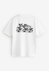 T-shirt en coton blanc avec un dessin graphique noir mettant en scène Félix le Chat et des personnages ludiques, comprenant des éléments roulants et du texte.