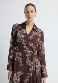 Mahagonifarbenes Wickelkleid aus glattem Stoff, mit einem cremefarbenen Paisleymuster, einem kragenlosen Ausschnitt und einem goldenen Knopfakzent.