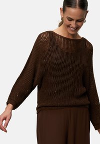 Bruine gebreide pullover met een losse, open weefstructuur. Heeft een brede halslijn en lange mouwen, gecombineerd met bijpassende bruine broek.