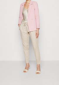 Lichtroze blazer, beige broek met elastische taille, crèmekleurige sandalen met gevlochten hakken en een satijnen cami-top. Eenvoudige, schone lijnen en zachte texturen.