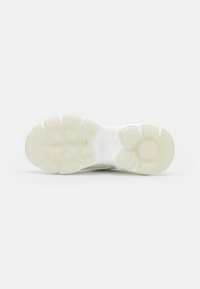 Sneaker sole in white rubber, featuring a textured pattern with hexagonal and rounded shapes for grip and traction. Flat, wide design.