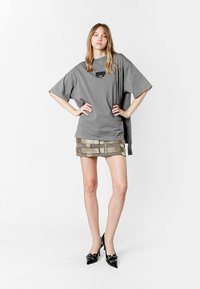 Camiseta gris de gran tamaño con un bolsillo en el pecho, combinada con una falda mini de caqui con un patrón que presenta franjas horizontales en capas y una cremallera. Tacones altos negros.