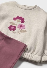 Maglione grigio chiaro con ricamo di fiori viola, abbinato a pantaloni bordeaux. Il maglione presenta polsini elasticizzati; tessuto morbido con una finitura testurizzata.
