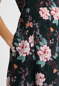 Abito floreale lunghezza ginocchio con uno sfondo verde scuro, peonie, fiori blu e dettagli. Realizzato in tessuto liscio con tasche laterali.