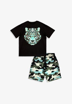 Chemise noire à manches courtes avec un motif géométrique de visage de tigre, associée à un short à motif camouflage dans des tons de vert, bleu, noir et blanc.