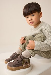 Braune High-Top-Schuhe mit zwei Klettverschlüssen, mit einem Hundemotiv an der Seite. Strukturierte Wildlederoptik mit Gummisohlen.