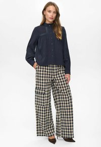 Woman wearing navy long-sleeve button-up blouse with lace details paired with high-waisted wide-leg beige and black checkered pants.