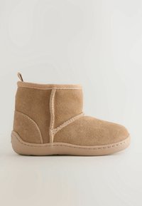 Bottine courte en daim beige avec bout arrondi, détails cousus, semelle plate en caoutchouc et languette à l'arrière.