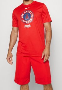 Conjunto atlético rojo que incluye una camiseta de manga corta con el logo de "Los Angeles Angels" y pantalones cortos a juego, fabricado en un tejido transpirable.