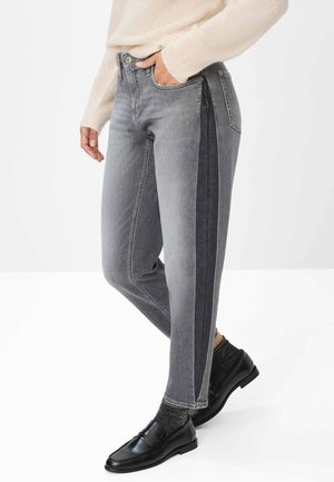 Jeans in denim grigio con gamba affusolata, pannelli laterali scuri a contrasto e cuciture sottili. Abbinati a scarpe nere e calzini grigi.