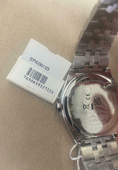 Hõbedane roostevabast terasest kell tekstureeritud randmeehtega, läbipaistva tagaküljega ja graveeritud logoga. Includes a tag with barcode and model number.