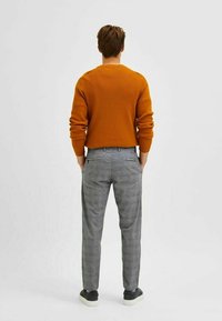 Orange textured sweater paired with gray checkered trousers. Casual shoes visible, with a smooth, neutral-colored sole. Rear view.