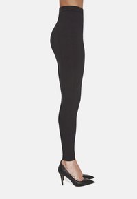 Czarne legginsy o wysokim stanie, o gładkiej fakturze i dopasowanym kroju, z pionowymi szwami, zestawione z czarnymi wysokimi szpilkami.