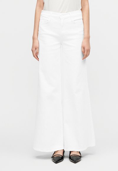 Άσπρο τζιν παντελόνι με φαρδιά λαιμόκοψη από τζιν ύφασμα, με ψηλή μέση και καθαρό φινίρισμα, συνδυασμένο με μυτερά μαύρα τακούνια για αντίθεση.